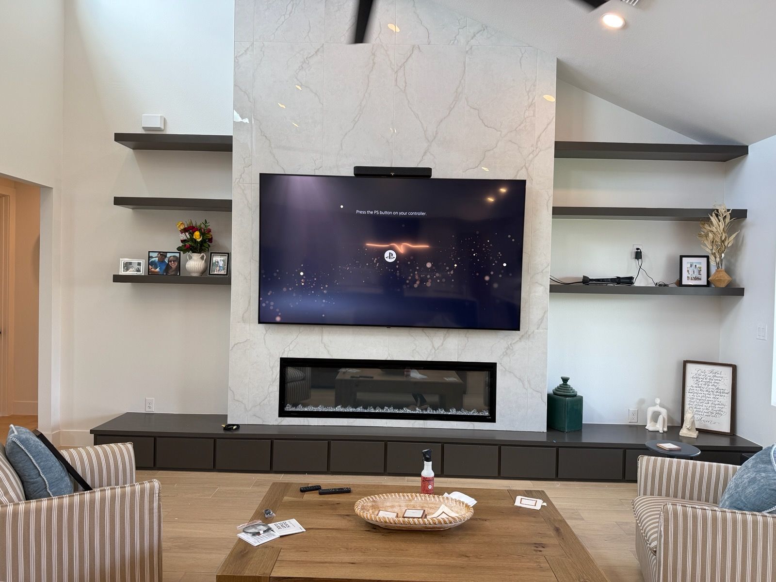 Modern living room with wall-mounted TV, fireplace, shelves, and striped chairs around a coffee table