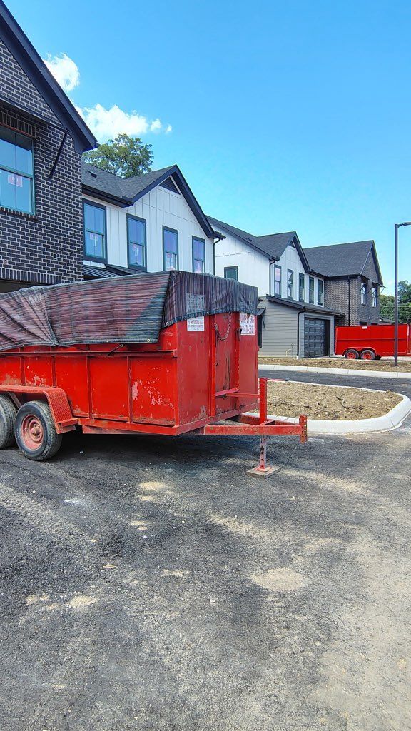 Red construction dumpster on a gravel lot beside modern white houses under a bright blue sky