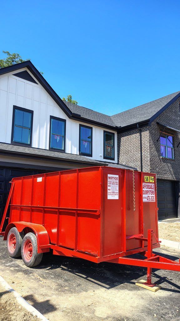 Bright red utility trailer parked beside a black-and-white house on a sunny day