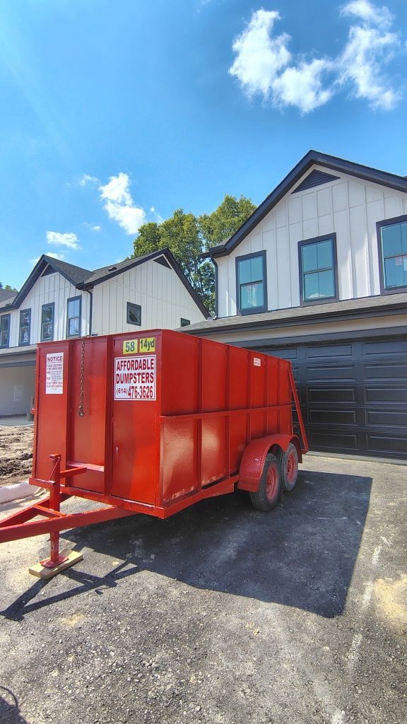 Red dumpster trailer parked in front of a house under a bright blue sky.