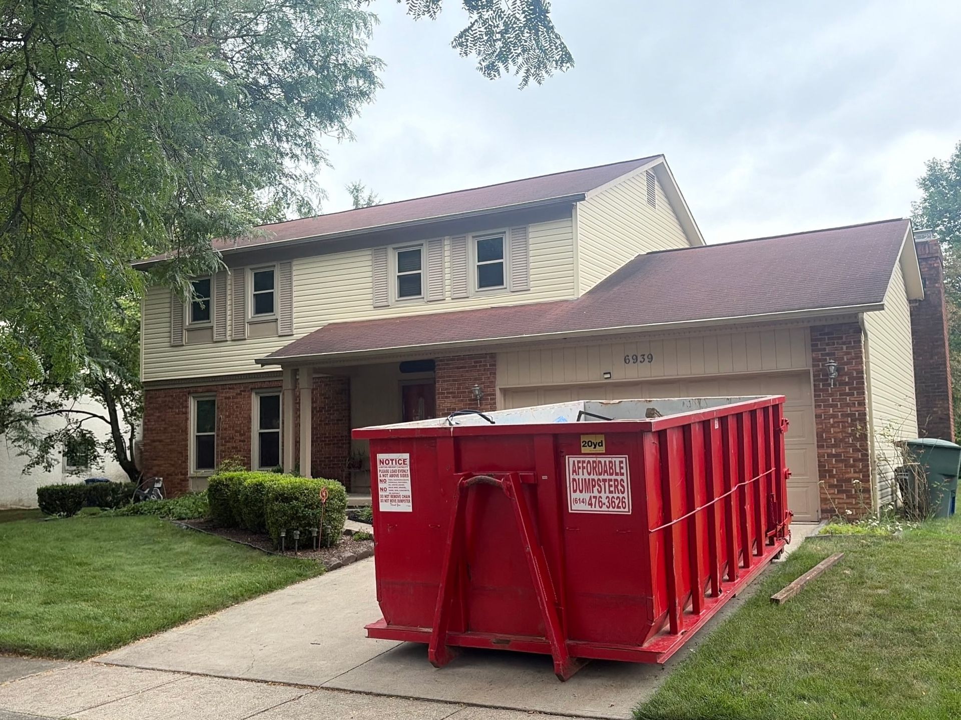 Red dumpster in front of a suburban house with a driveway and lawn