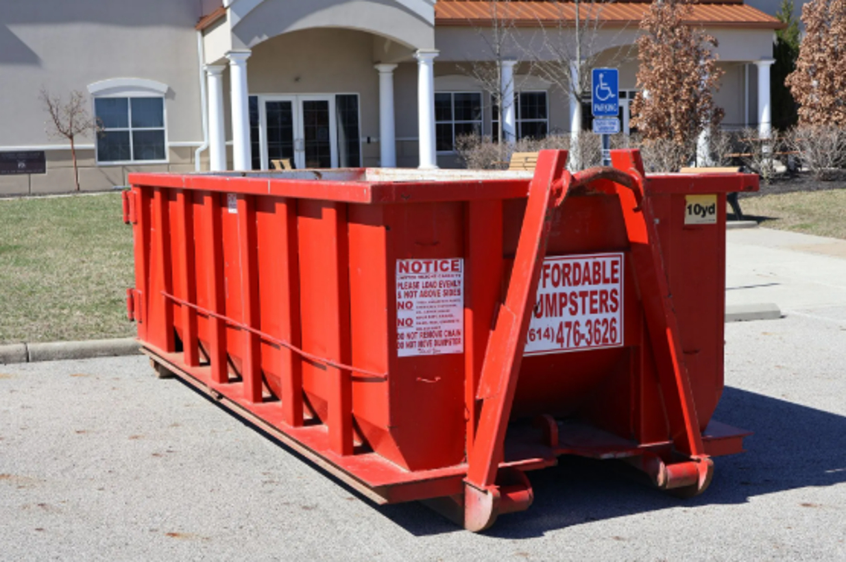 Red 10 yard dumpster rental container placed on a paved lot for a cleanout project.