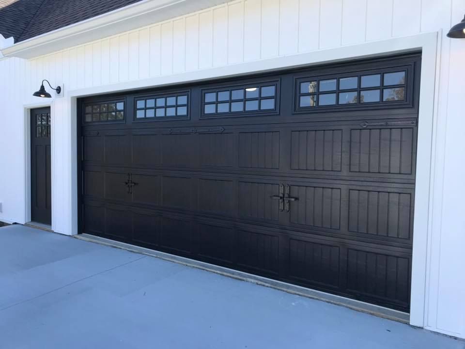 A black garage door is on a white house.