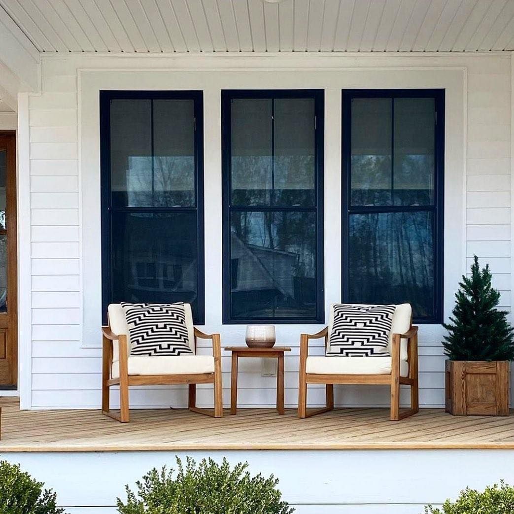 Two chairs and a table on a porch with three windows