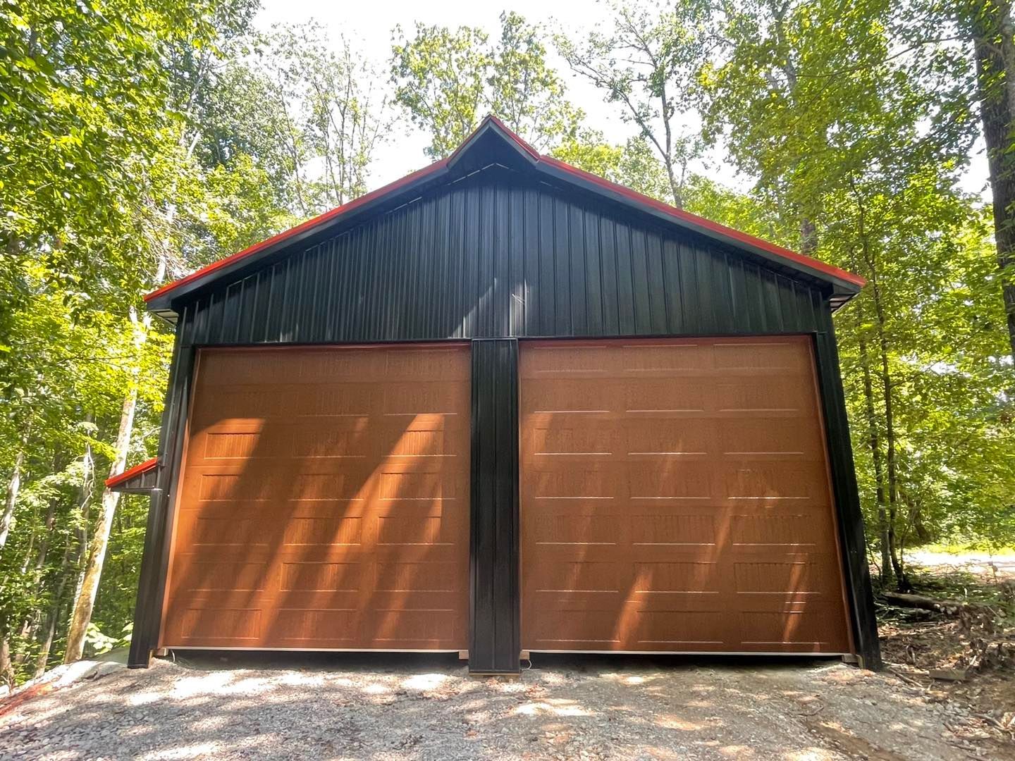 A garage with a red roof and wooden doors is surrounded by trees.