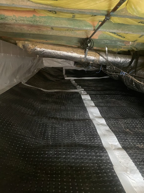 A picture of a crawl space with a drainage mat on the floor.