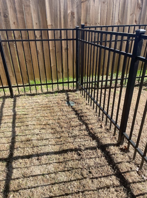 A metal fence with a wooden fence in the background.