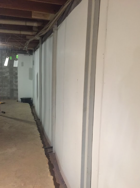 A long hallway in a basement with white walls and a wooden floor.