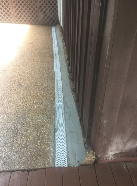 A drain on the side of a building next to a wooden deck.