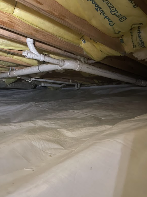 A bunch of pipes are hanging from the ceiling of a basement.