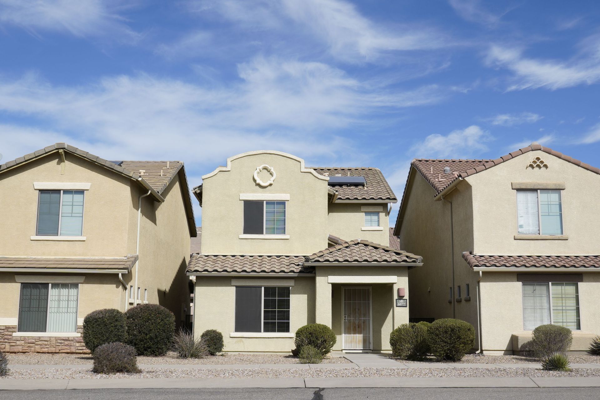 Row of beige stucco townhouses under a blue sky with desert landscaping