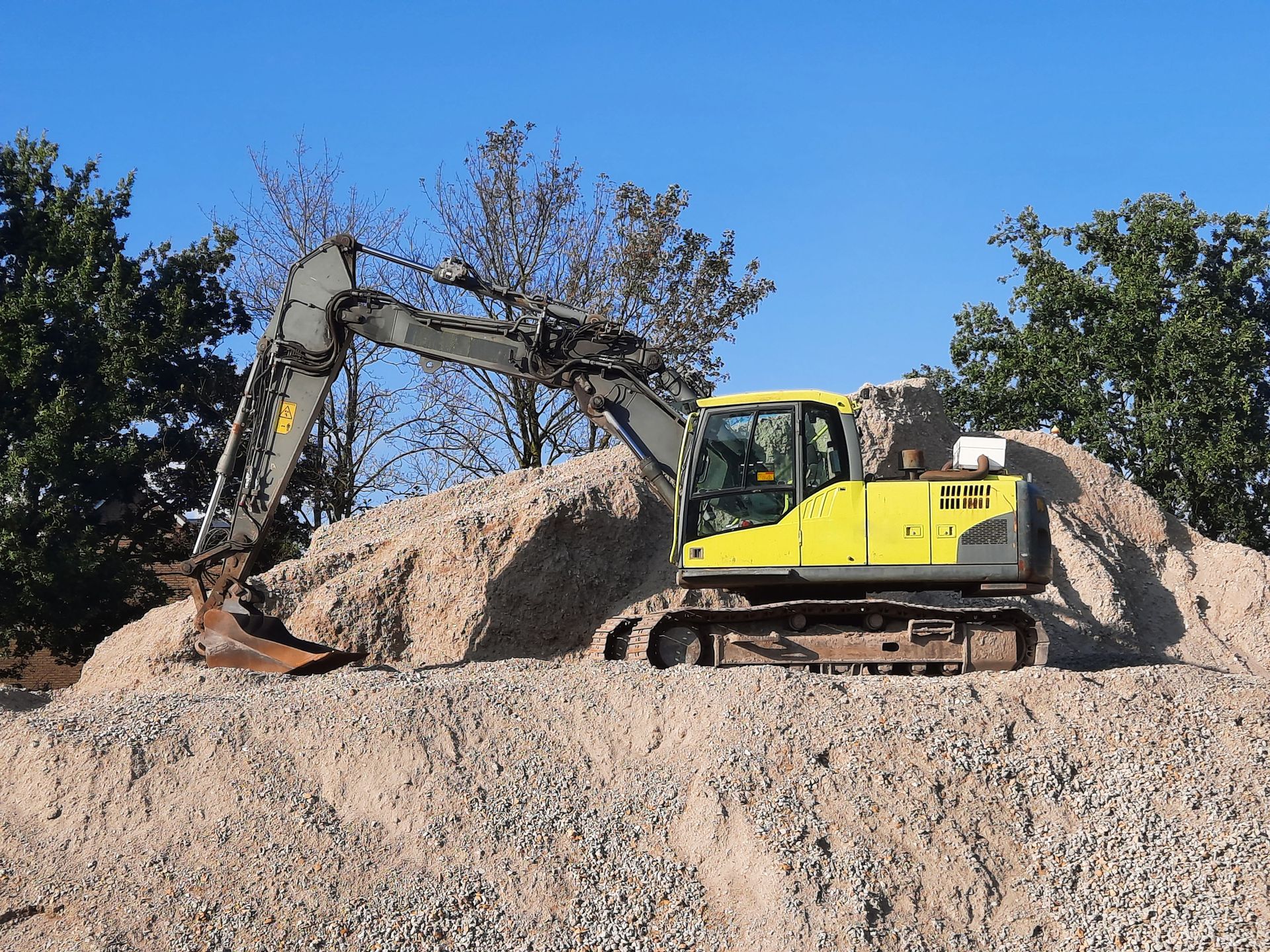 Yellow excavator loading dirt in a rocky construction site under a blue sky