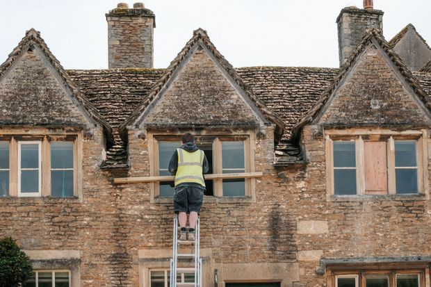 Worker on a ladder repairing a brick building’s upper window from outside