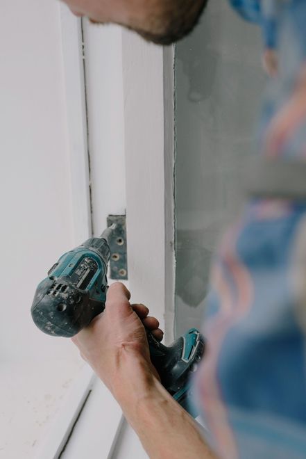 Person using a teal power drill to install a metal bracket on a white door frame