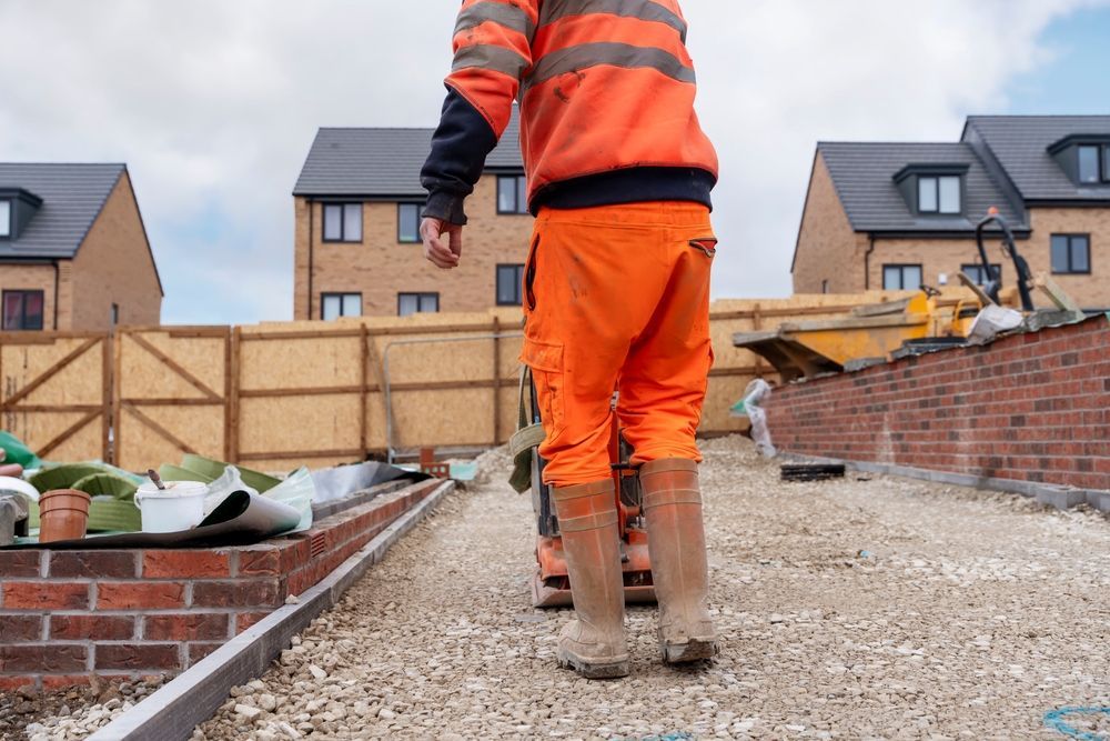 Construction worker in orange safety gear walking on gravel path at a housing site