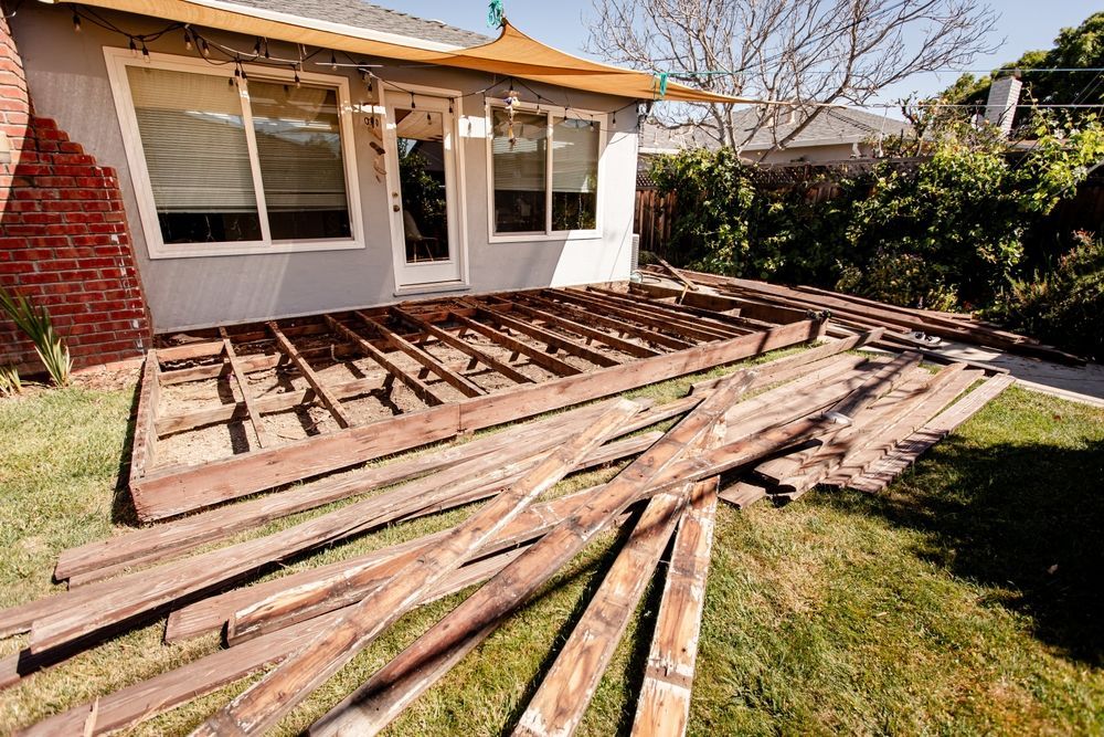 Backyard deck under construction with exposed wooden joists and stacked boards beside a house.