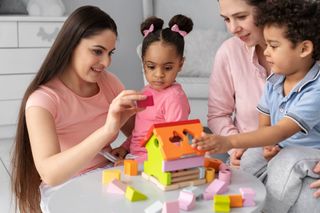Two women and two children are playing with wooden blocks at a table.