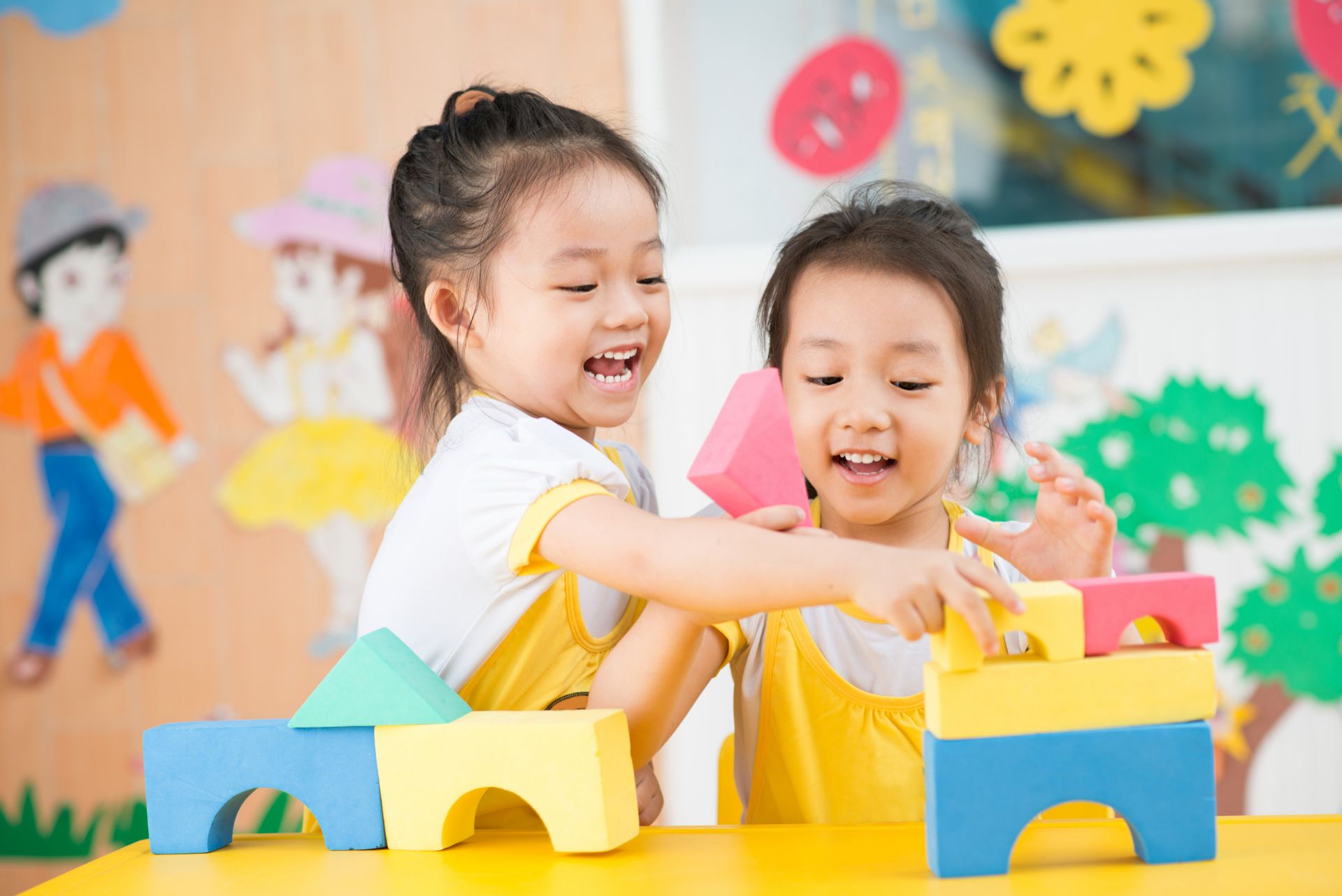 Two little girls are playing with blocks at a table.