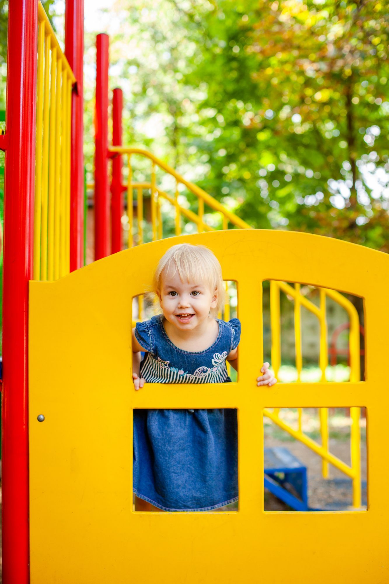 A little girl in a blue dress is playing on a playground.