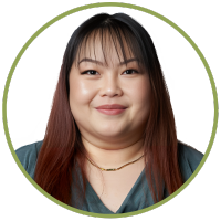 A photo of a smiling asian woman with long dark hair and a teal v-neck shirt with a gold neclace.