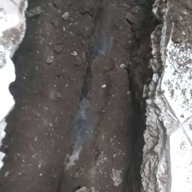Una zanja estrecha con tierra oscura entre muros de hormigón blanco o de piedra.
