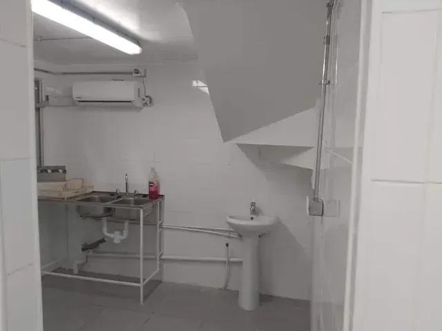 Pequeño baño blanco con lavabo de pedestal, mesa de metal y techo inclinado debajo de las escaleras.