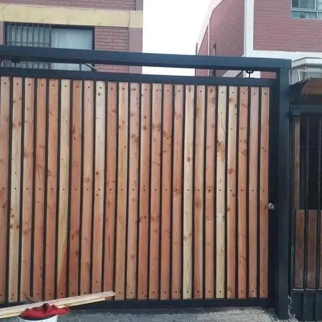 Puerta de entrada de listones de madera con marco de metal negro y un pequeño objeto rojo en el suelo.