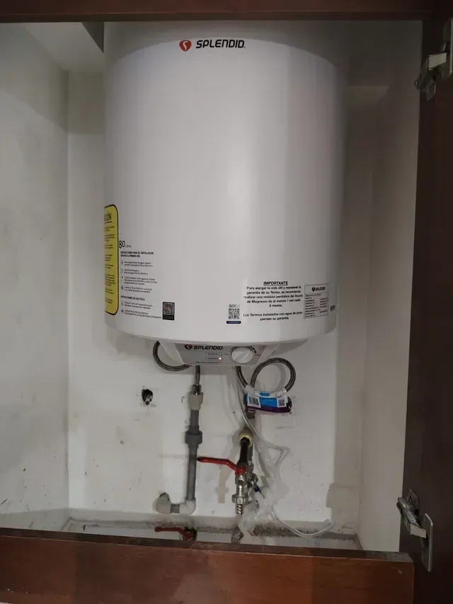 Calentador de agua blanco montado sobre tuberías expuestas en un cuarto de servicio.