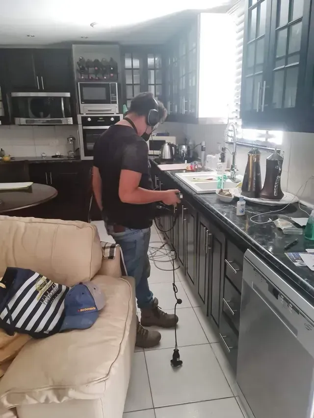 Una persona cocina en una cocina luminosa junto a un sofá beige y encimeras negras.