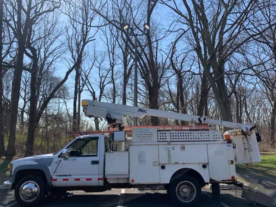 A white bucket truck parked in a paved lot, with bare trees in the background under a blue sky.