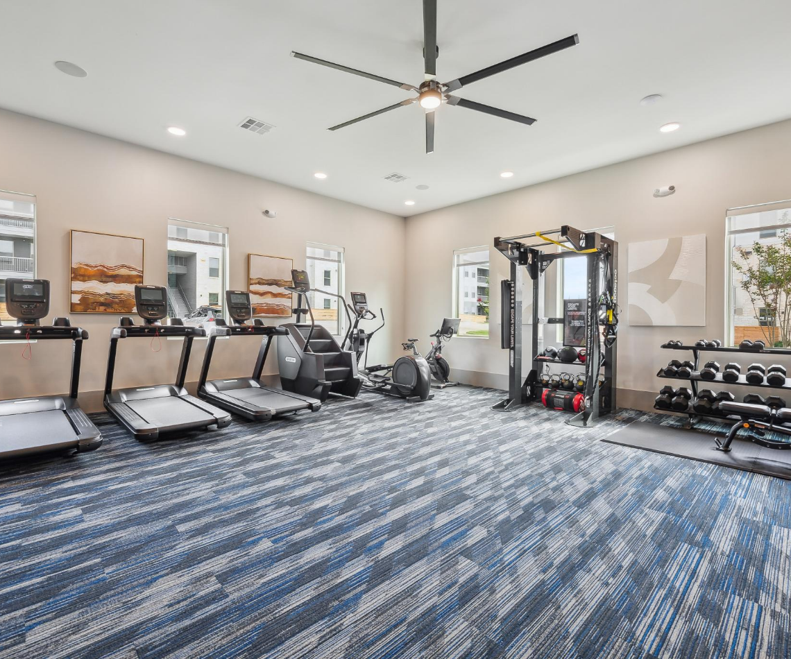 A large gym with treadmills , exercise bikes , and a ceiling fan.