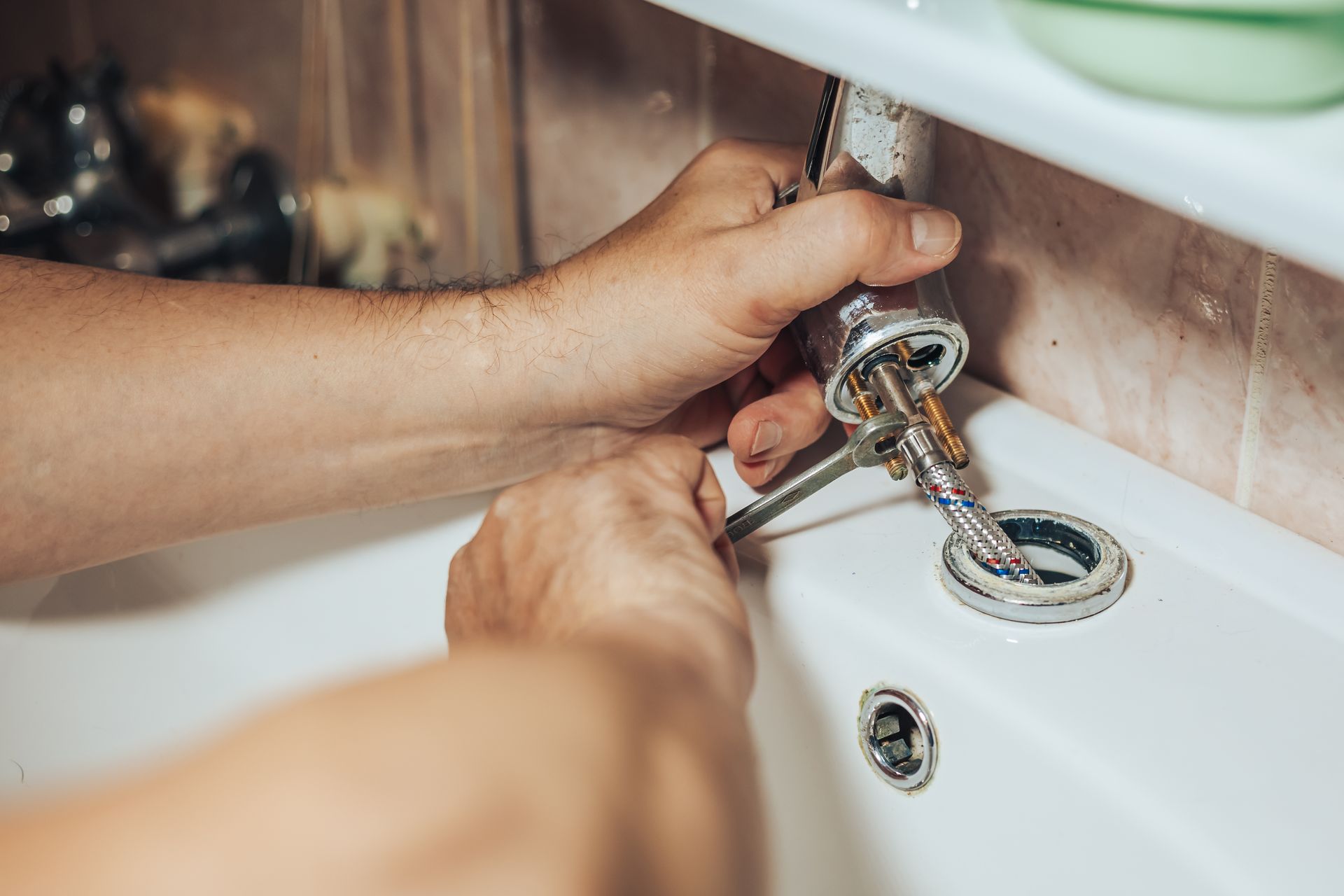 The hands of a plumber servicing a leaky old tap on the tap in the bathroom.