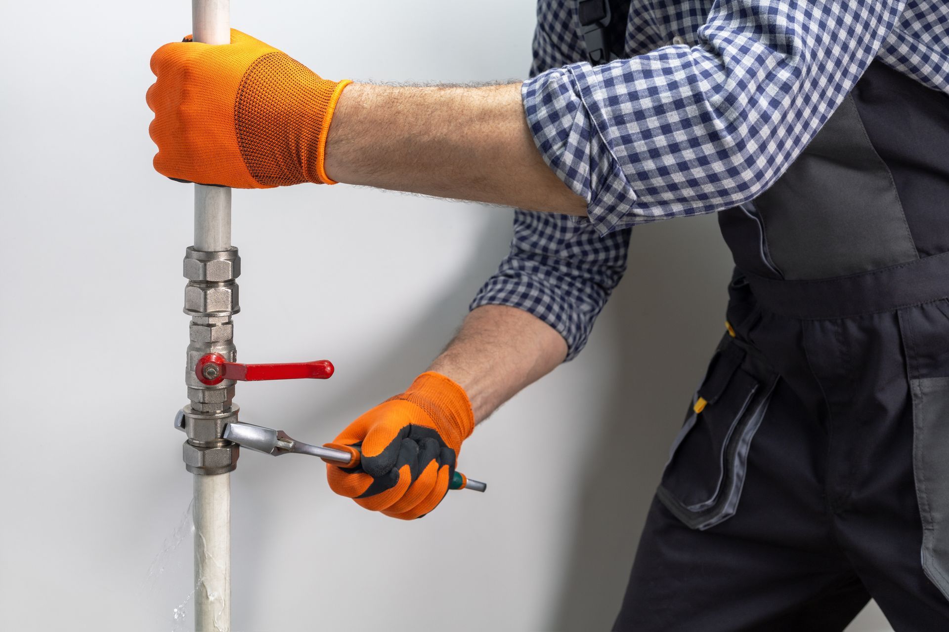 A plumber in uniform is working on a pipe that is dripping water. A plumber in uniform is working on a pipe that is dripping water.