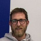 Un uomo con la barba e gli occhiali sorride alla telecamera.