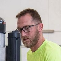 Un uomo con la barba e gli occhiali sta lavorando a una macchina.