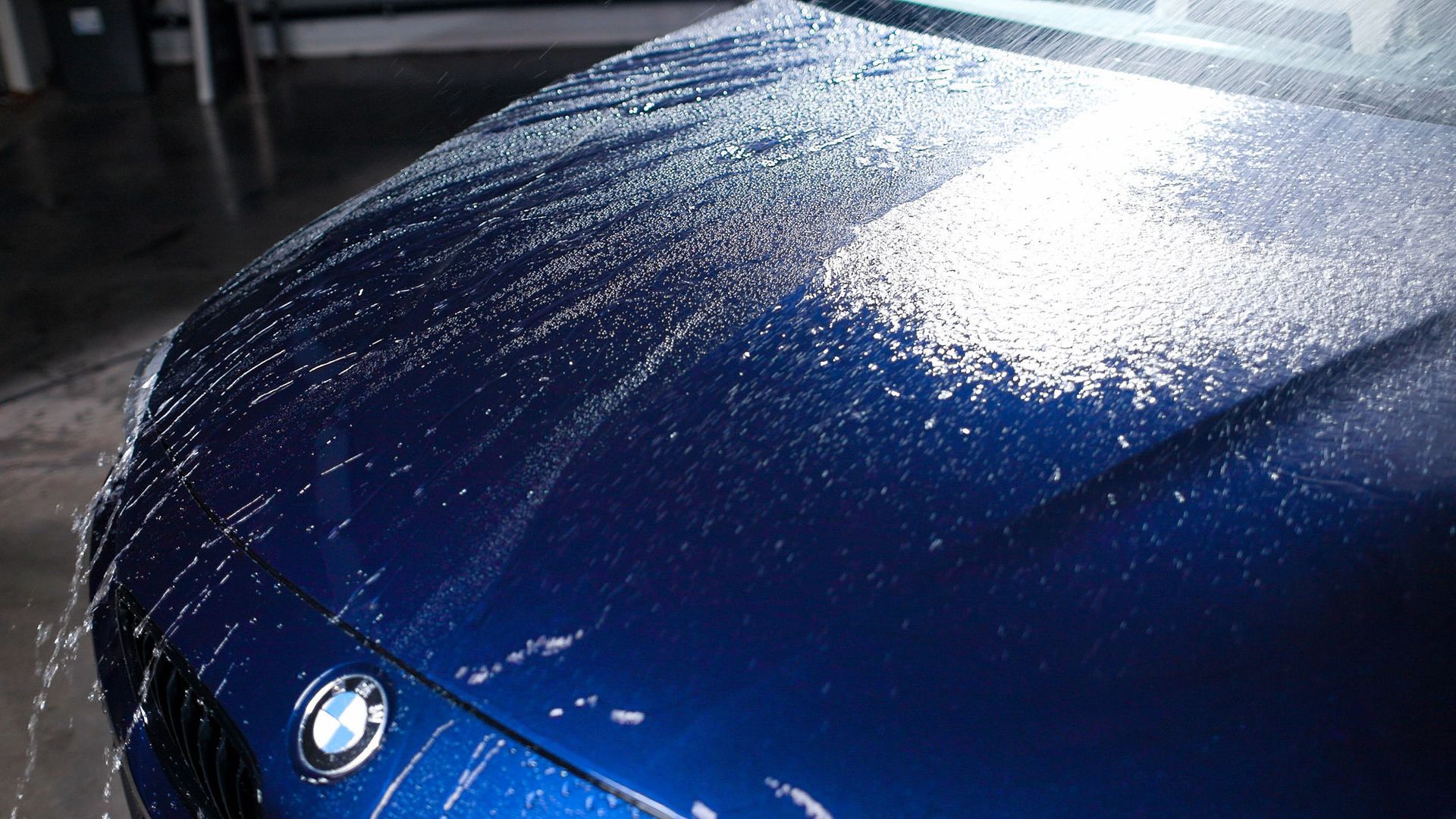 The hood of a blue bmw is covered in water.