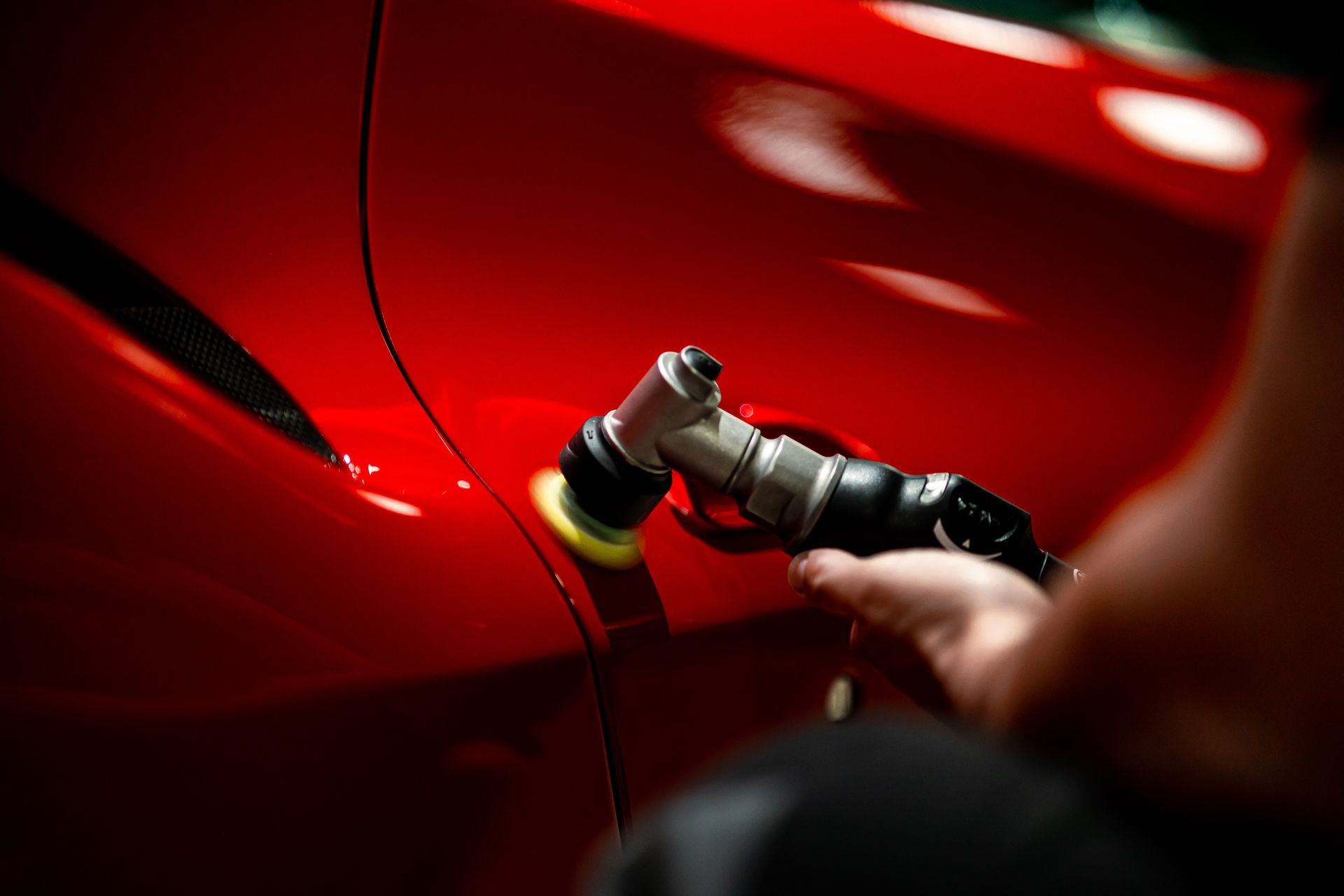 A person is polishing a red car with a machine.