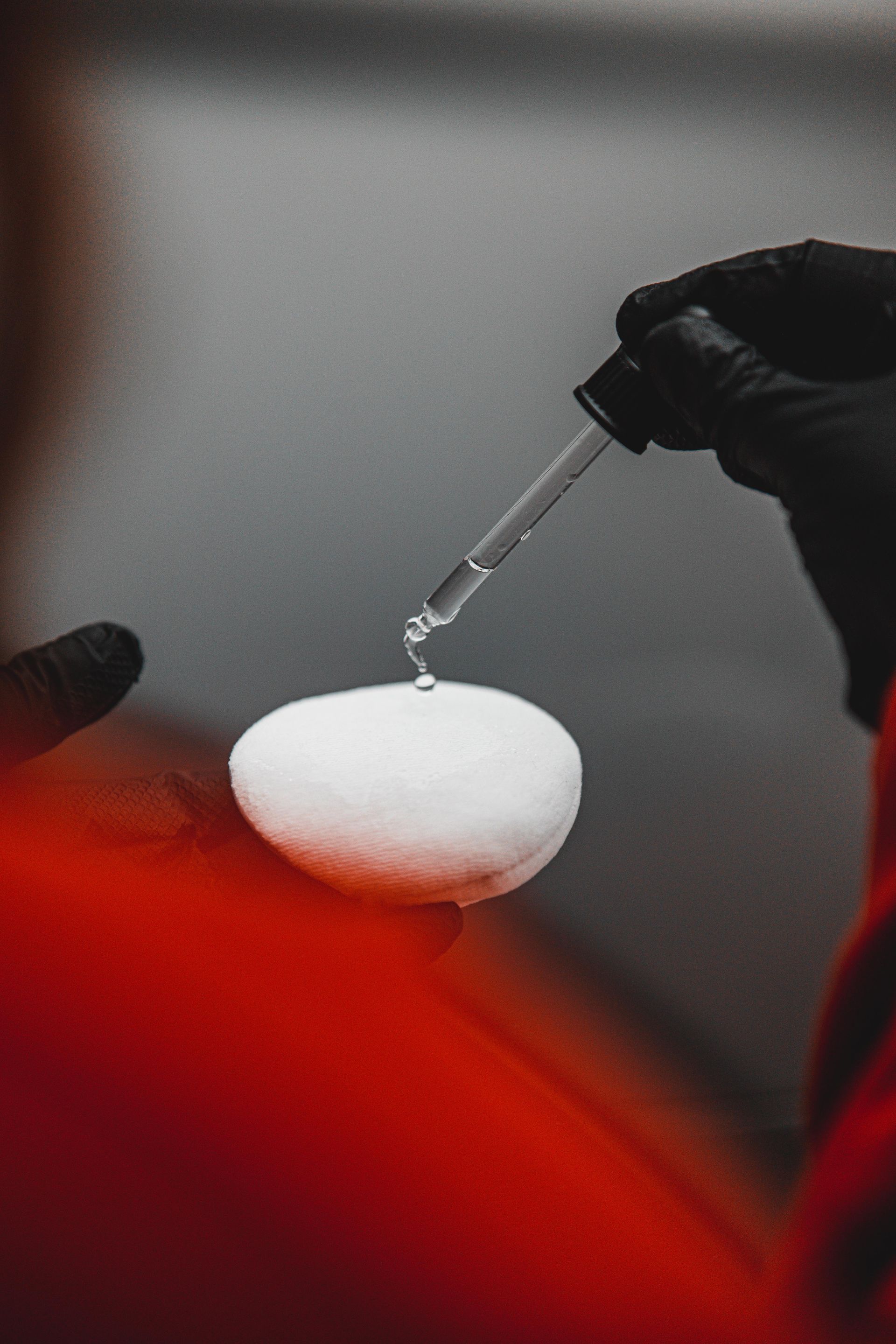 A person is holding a pipette over a white object.