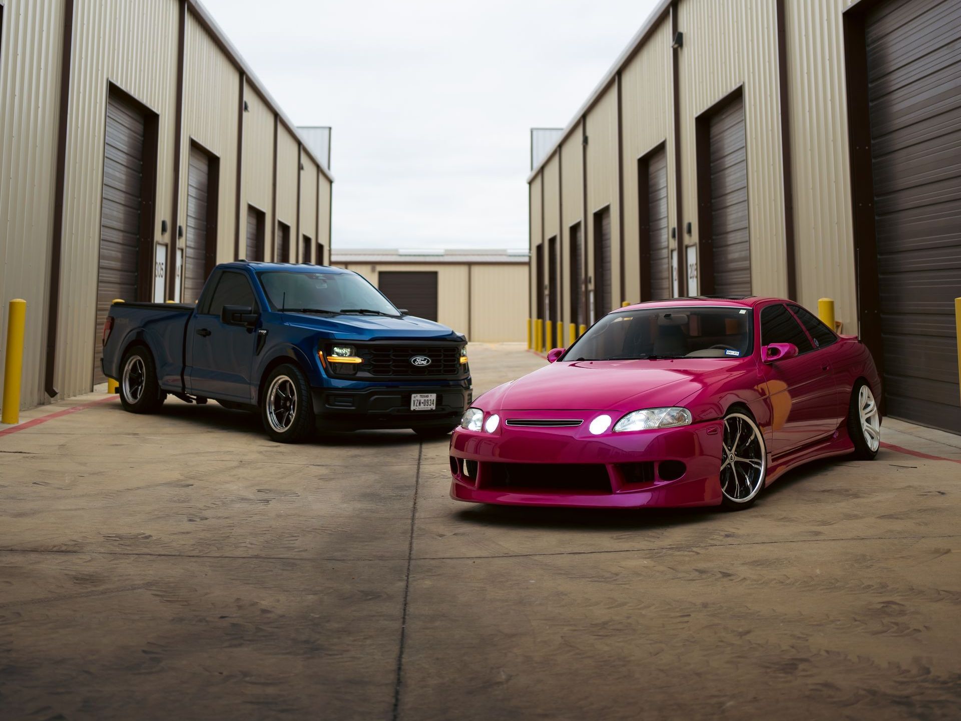 A blue truck and a pink car are parked next to each other in a parking lot.