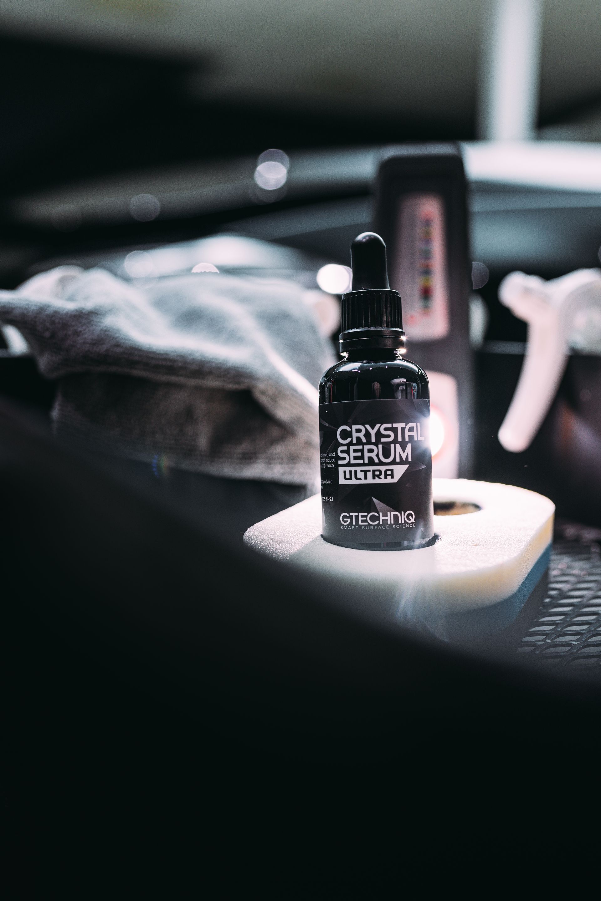 Black serum bottle on a sponge, car detailing products in a garage setting.