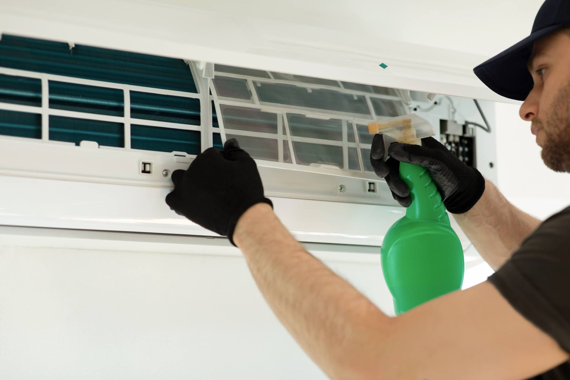 Tecnico che pulisce un condizionatore d'aria a parete con un flacone spray verde e un panno.