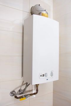 Scaldabagno a gas bianco a parete con tubi a vista, installabile in un bagno piastrellato o in un locale di servizio.