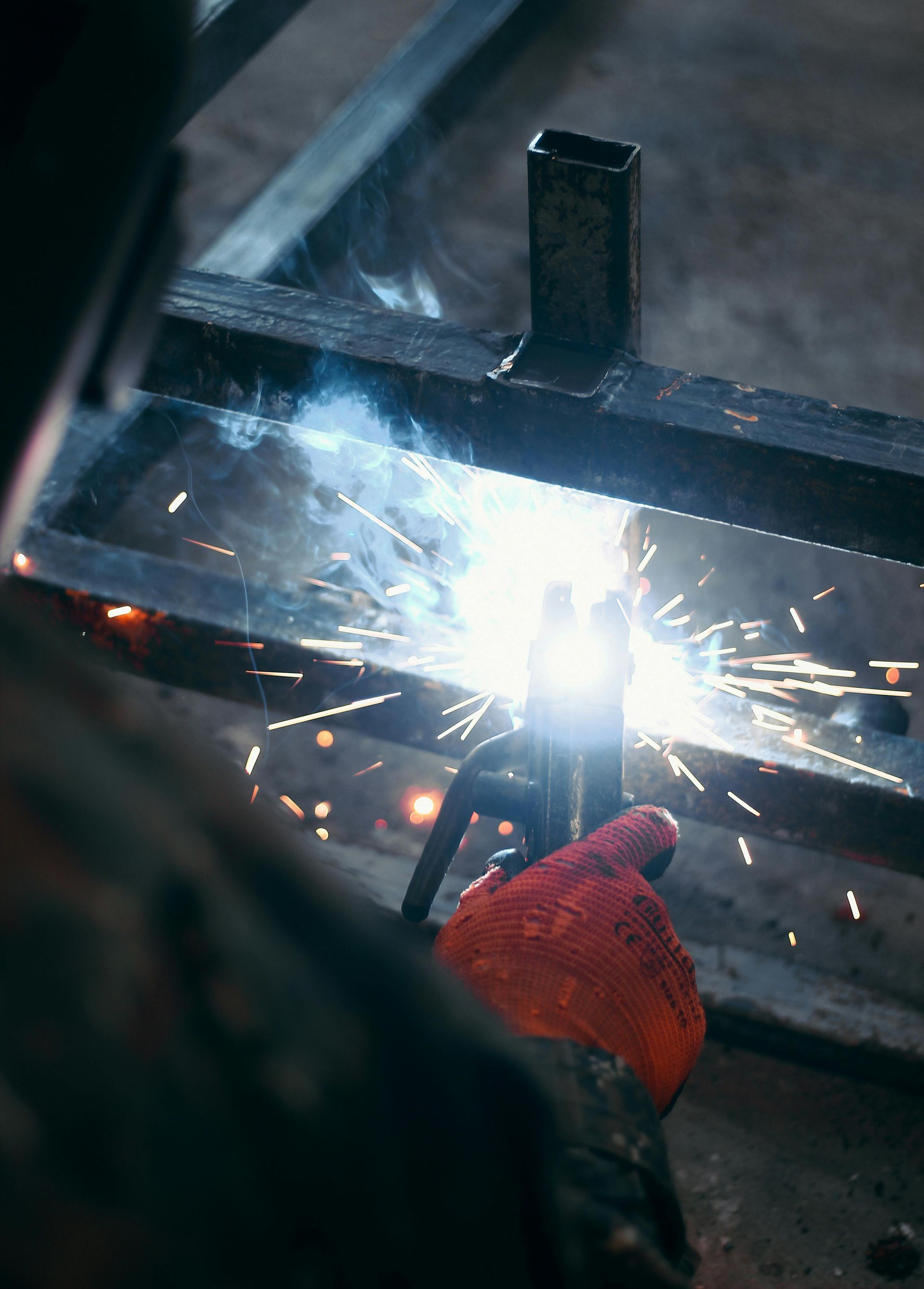 Welder wearing red glove, welding metal frame, sparks flying.