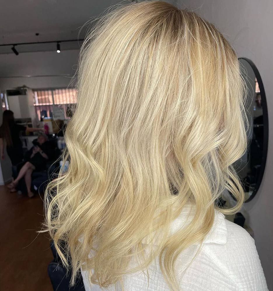 A Woman With Blonde Hair is Standing in Front of a Mirror in a Salon — Hairenvy in Ettalong Beach, NSW