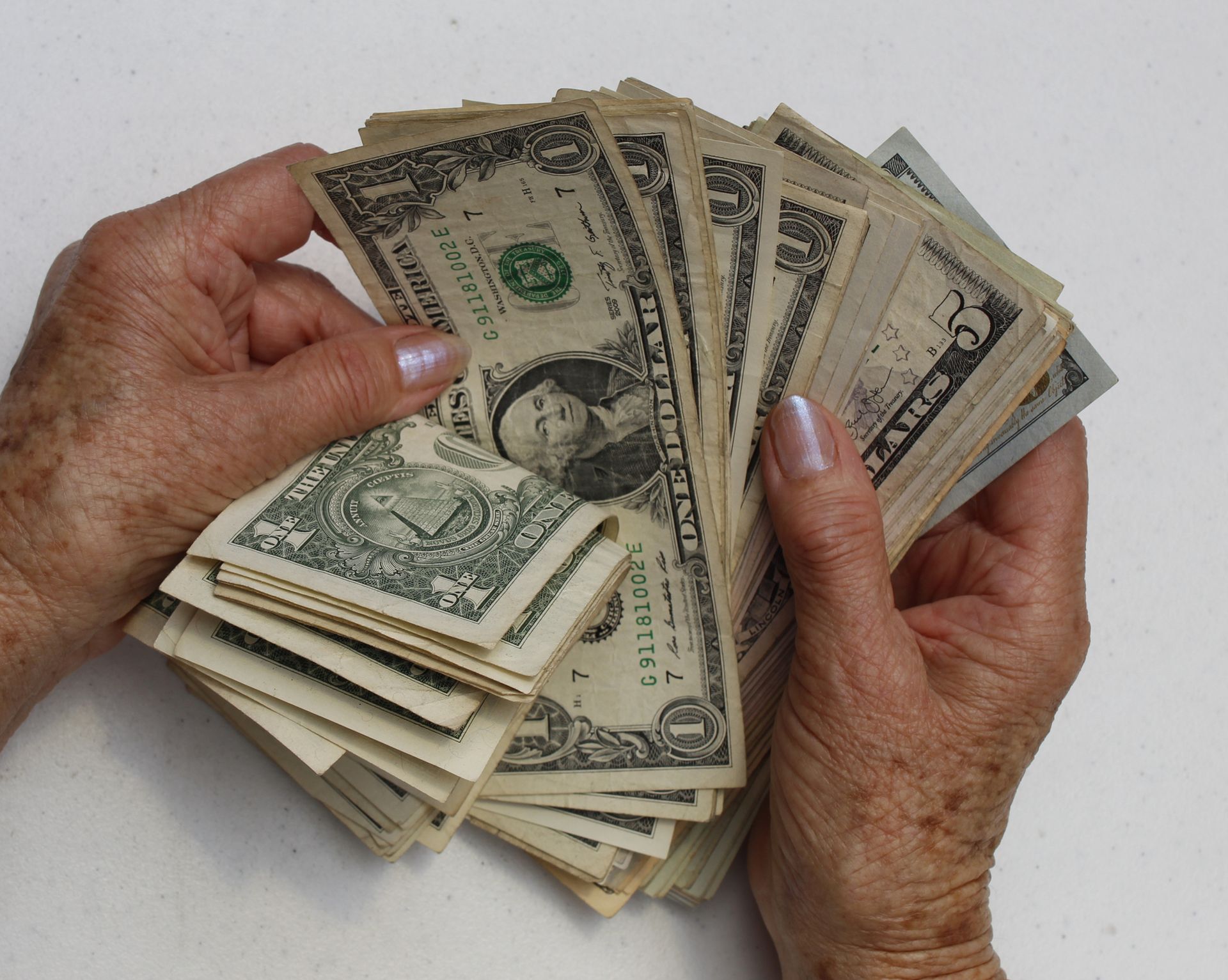 A person is holding a stack of one dollar bills
