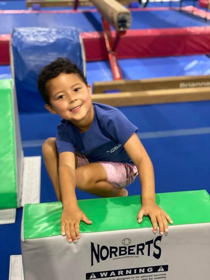 A young boy is sitting on a norberts block in a gym.