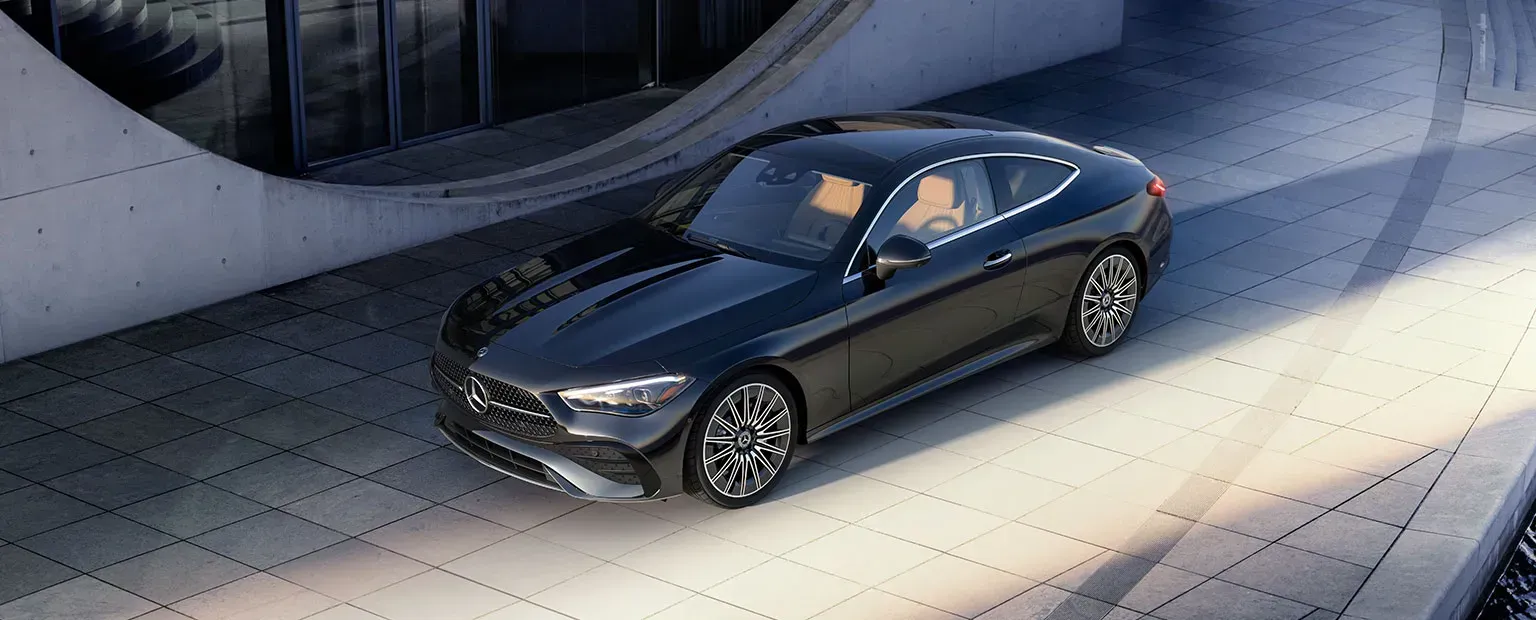 A black Mercedes-Benz coupe parked on a textured concrete surface. The interior features tan leather seats.