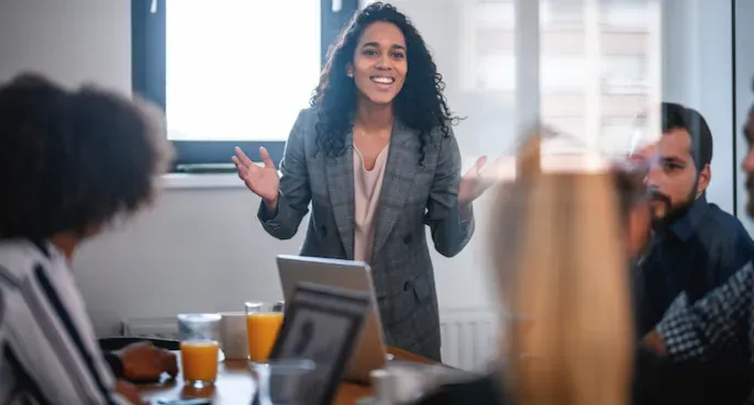 Woman presenting in a conference room while seated colleagues watch and listen.