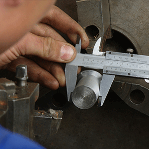 Una mano usando un calibrador para medir un cilindro de metal en un taller.
