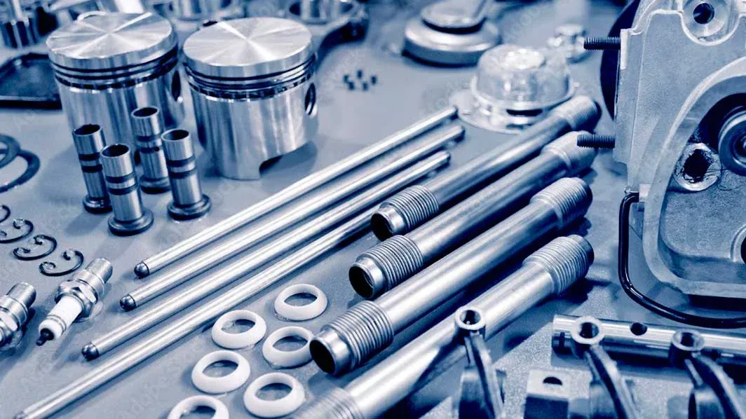 Varias piezas metálicas de motor y tornillos dispuestos sobre una superficie industrial de color azul.